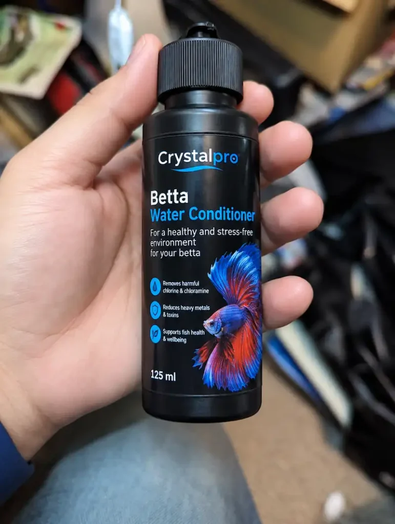 Crystalpro Betta Water Conditioner bottle held in hand, showing the Betta Water Conditioner label and blue-red betta fish design.
