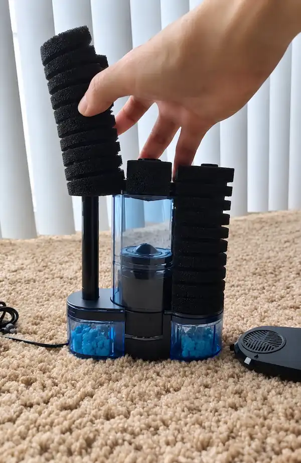 Hand adjusting the black foam components of a black and blue aquarium filter during cleaning